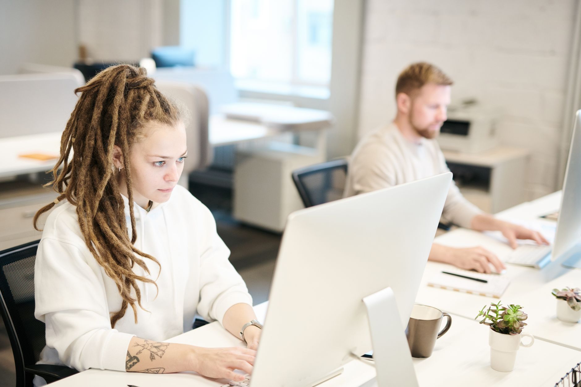 Deux collègues concentrés sur leur travail, utilisant des ordinateurs dans un bureau moderne et lumineux.